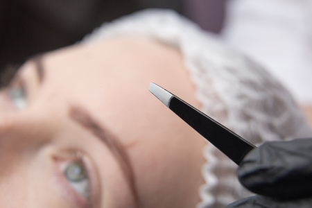 Young woman plucking eyebrows with tweezers closeの写真素材