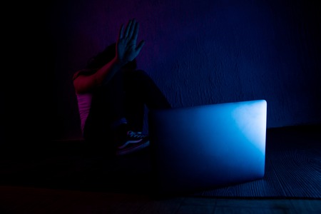 scared and sad female teenager with computer laptop suffering cyberbullying and harassment being online abused by stalker or gossip feeling desperate and humiliated in cyber bullying.の写真素材