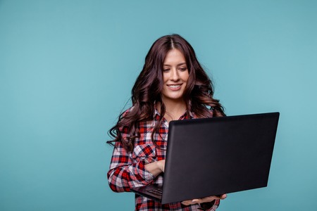 Portrait of an excited young girl holding laptop computer and celebrating success isolated over blueの写真素材