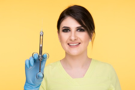 Closeup photo of female dentist holding oral syringe isolated over the yellow backgrownd.の写真素材