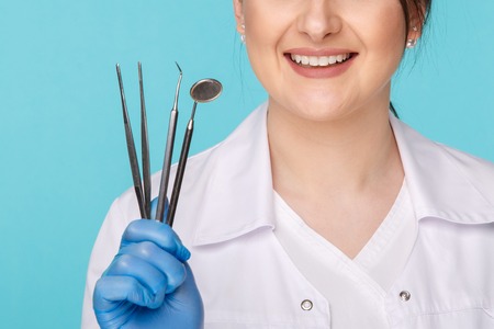 Handsome brunette dentist with tools isolated over the blue background.の写真素材