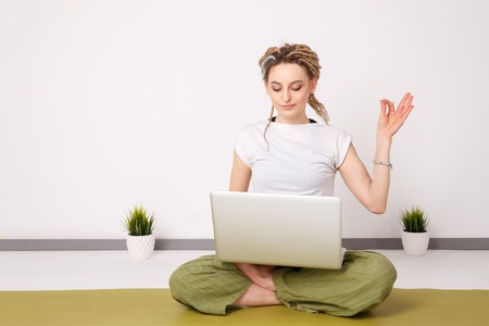 Having a rest in office. Yoga at work. Typing on the laptop and doing lotus pose.の写真素材