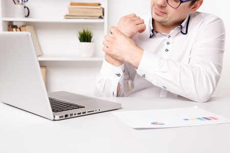 Illness hands of young businessman. Tired working on a laptop.