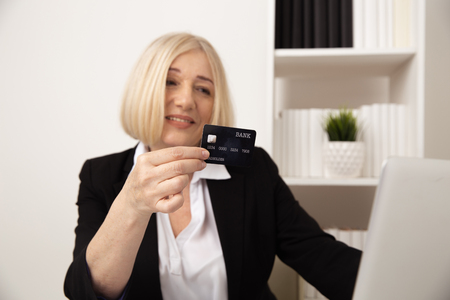 Blonde woman holding black credit card infront of computer.の写真素材