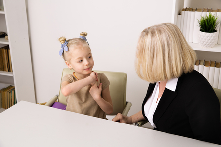 Female psychologist with little kid patient sitting indoor at the desk and talking. Child problem concept.の写真素材