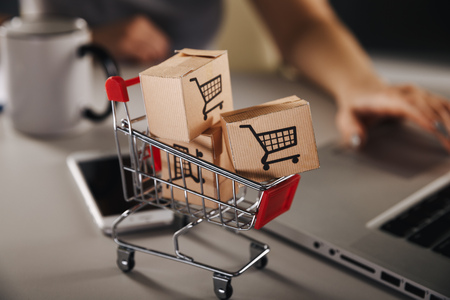 Online shopping . ecommerce and delivery service concept : Paper cartons with a cart or trolley logo on a laptop keyboard, depicts customers order things from retailer sites via the internetの写真素材