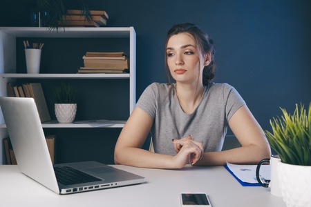 Problem in office. Tired female worker at the desk sitting and thinking infront of computer.の写真素材