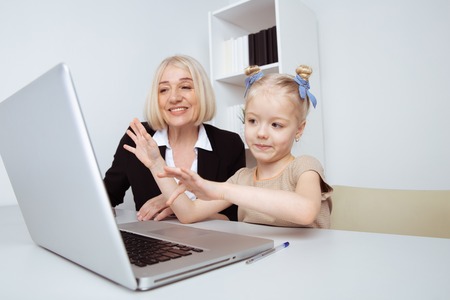 Girl with grandmother sitting on the desk and learning something by computer.の写真素材