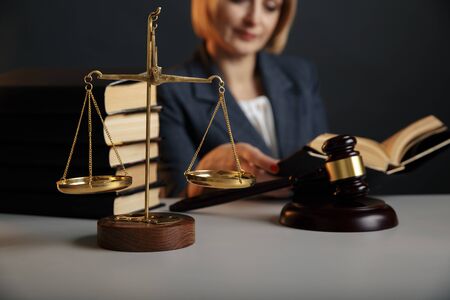 Juridical concept. Closeup picture of reading woman. Gavel and scale on the table.の写真素材