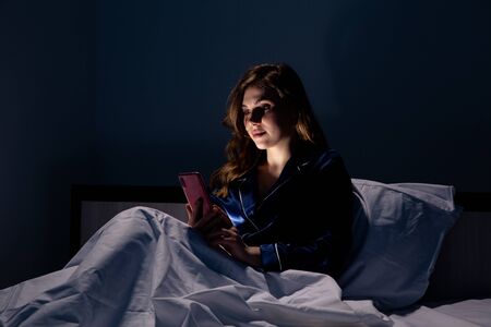 Beautiful woman working on the phone sitting in the bed.の写真素材