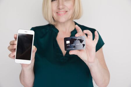 Photo of smiling adult lady with mobile and credit card in her hands.