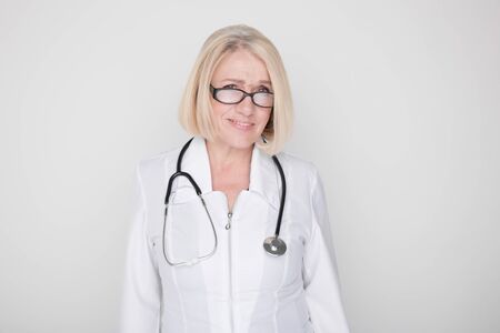 Portrait of happy professional female medical worker standing in a studio with stethoscope on her neck.の写真素材