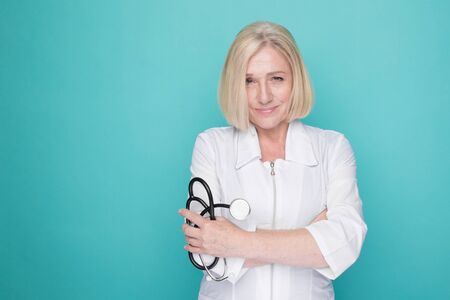 Woman in a white medical clothes standing isolated on a blue background and holding stethoscope in her hand.の写真素材