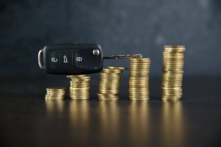 Close-up Of Car Key In Front Of Coins Stacked On Wooden Tableの写真素材