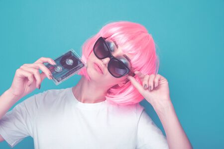 90s girl fashion concept. Woman in glasses holding audio cassette in a blue studio.