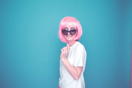 Young woman in a pink wig and dark glasses isolated in a studio.の写真素材