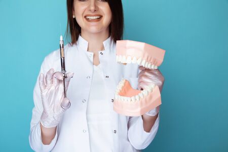 Portrait of female dentist with fake jaw and dental syrigne isolated.