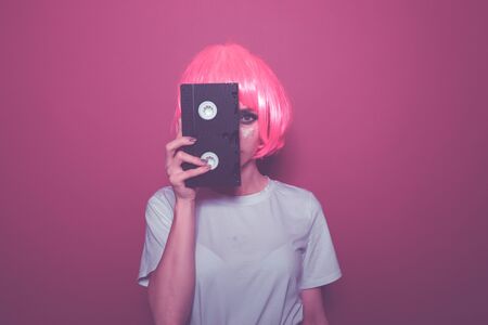 Young girl in the pink wig closing her eye by an old cassette.
