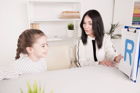 Child with therapist working on pronunciation and sounds together sitting in the class.
