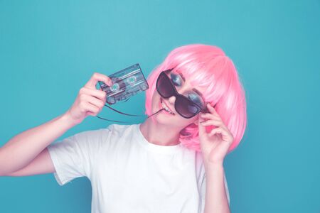 90s girl fashion concept. Woman in glasses holding audio cassette in a blue studio.の写真素材