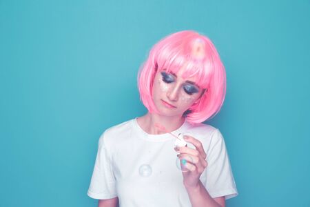 Happy woman blowing soap bubble in a blue studio.の写真素材