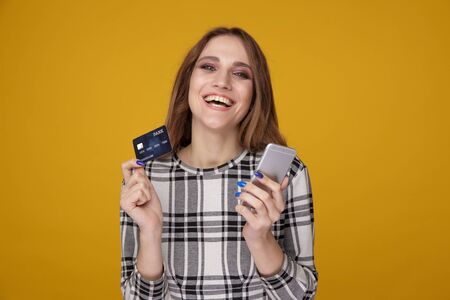 Handsome woman showing credit card and using cellphone standing isolated.