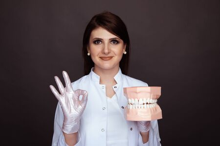 Brunette female doctor in the white gloves and uniform holding jaw isolated.