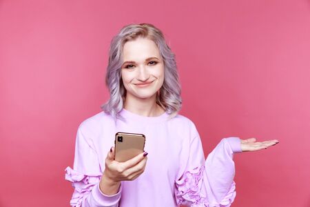 Happy girl using phone and smiling standing in the pink studio.の写真素材