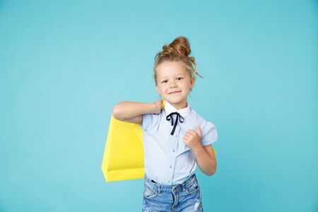 Little cute and funny girl holding big bright colored yellow paper bags in the blue studio.の写真素材