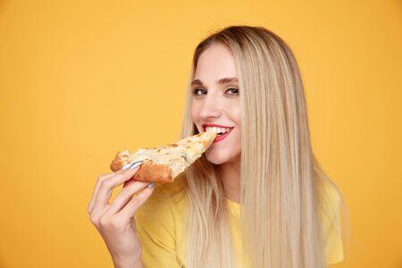 Happy girl with delicious cheese pizza isolated over the yellow background.の写真素材