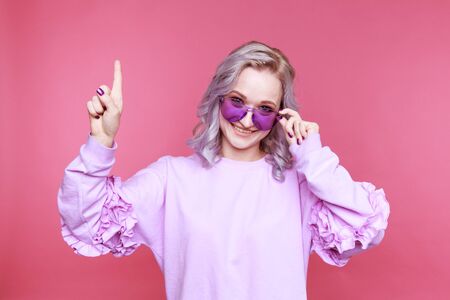 Happy blond model showing by finger up sstanding in the pink studio isolated.の写真素材