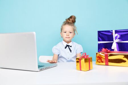 Sweet little girl siting at the desk with a lot of xmas gifts and the laptop.