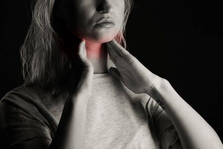Female checking thyroid gland by herself. Close up of woman in white t- shirt touching neck with red...