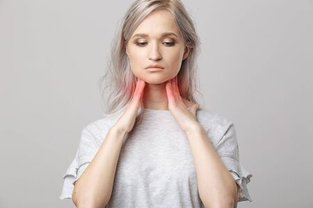 Female checking thyroid gland by herself. Close up of woman in white t- shirt touching neck with red spot. Thyroid disorder includes goiter, hyperthyroid, hypothyroid, tumor or cancer. Health care.の写真素材