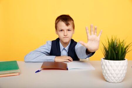 Angry pupil showing stop sign sittin isolated in the class.