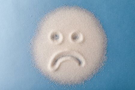 Salt scattered on black surface. Drawn sad face. Concept- diet, harm to health from excessive consumption of salt and sugar.の写真素材