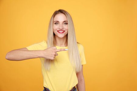 Happy woman model in the yellow T-shurt with red lips pointing to the side isolated.の写真素材