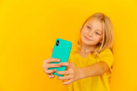 Smiling little girl kid showing blue screen of new popular mobile phone on light yellow background.の写真素材