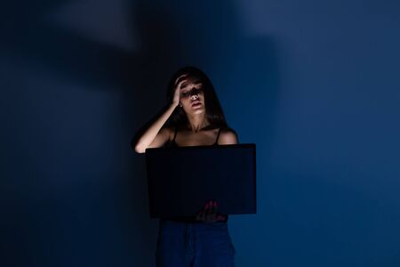 sad and female teenager with tablet computer and laptop suffering cyberbullying and harassment being online abused by stalker or gossip feeling desperate and humiliated in cyber bullying.の写真素材