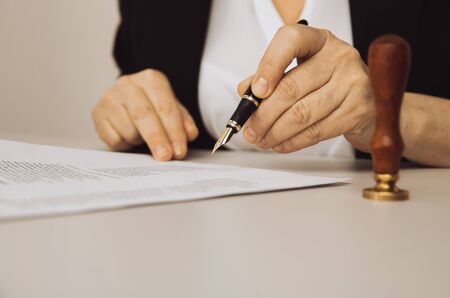 Closeup view of female hand holding pen. Paper and stamp on the deskの写真素材