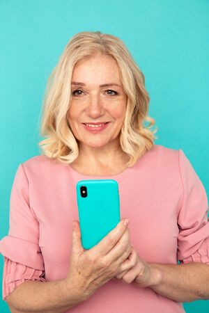 Happy mature woman holding blue phone in the studio isilated.