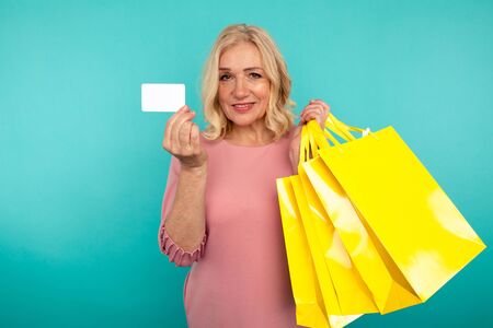 Female person on the blue background holding credit card and many yellow shopping bags.