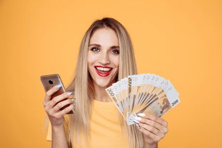 Happy girl with mobile and cash isolated on the yellow background.