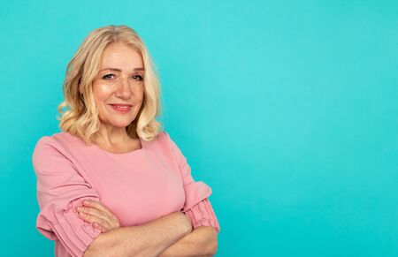 Blond adult female posing in the pink dress isolated over the blue studio.