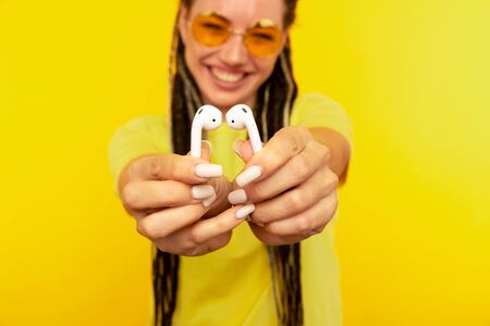 Listening music on airpods. Woman in the yellow studio with white airpods.