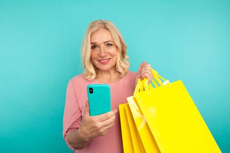 Happy adult female holding phone and yellow bags.