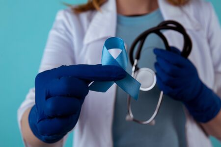 Doctor holding blue awareness ribbon, closeup view. Symbol of medical issues.