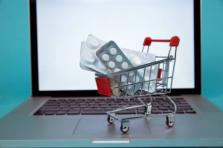 Mini shopping cart full of homeopathic remedies on laptop background. Homeopathy and internet online...