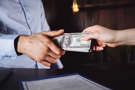 Man offering batch of hundred dollar bills. Hands close up. Venality, bribe, corruption concept. Hand giving money - United States Dollars or USD . Hand receiving money from businessman.の写真素材