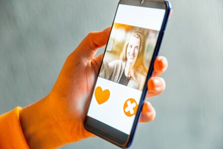 Online dating app in smartphone. Man looking at photo of beautiful woman. Person swiping and liking profiles on relationship site or application. Single guy searching for love partner. Mockup website.の写真素材